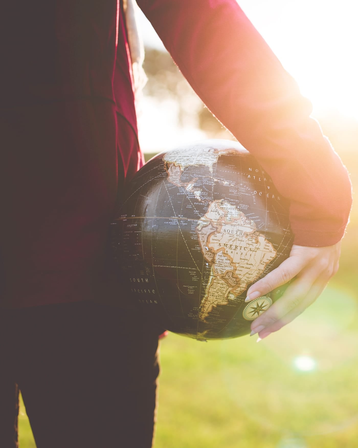 Person holding a world globe under one arm in a sunlit field