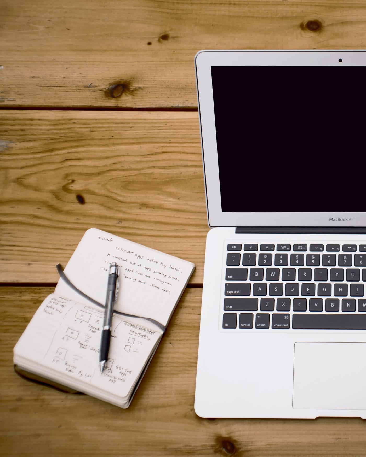 Open laptop, notebook with pen, and a smartphone laid out on a wooden table seen from above