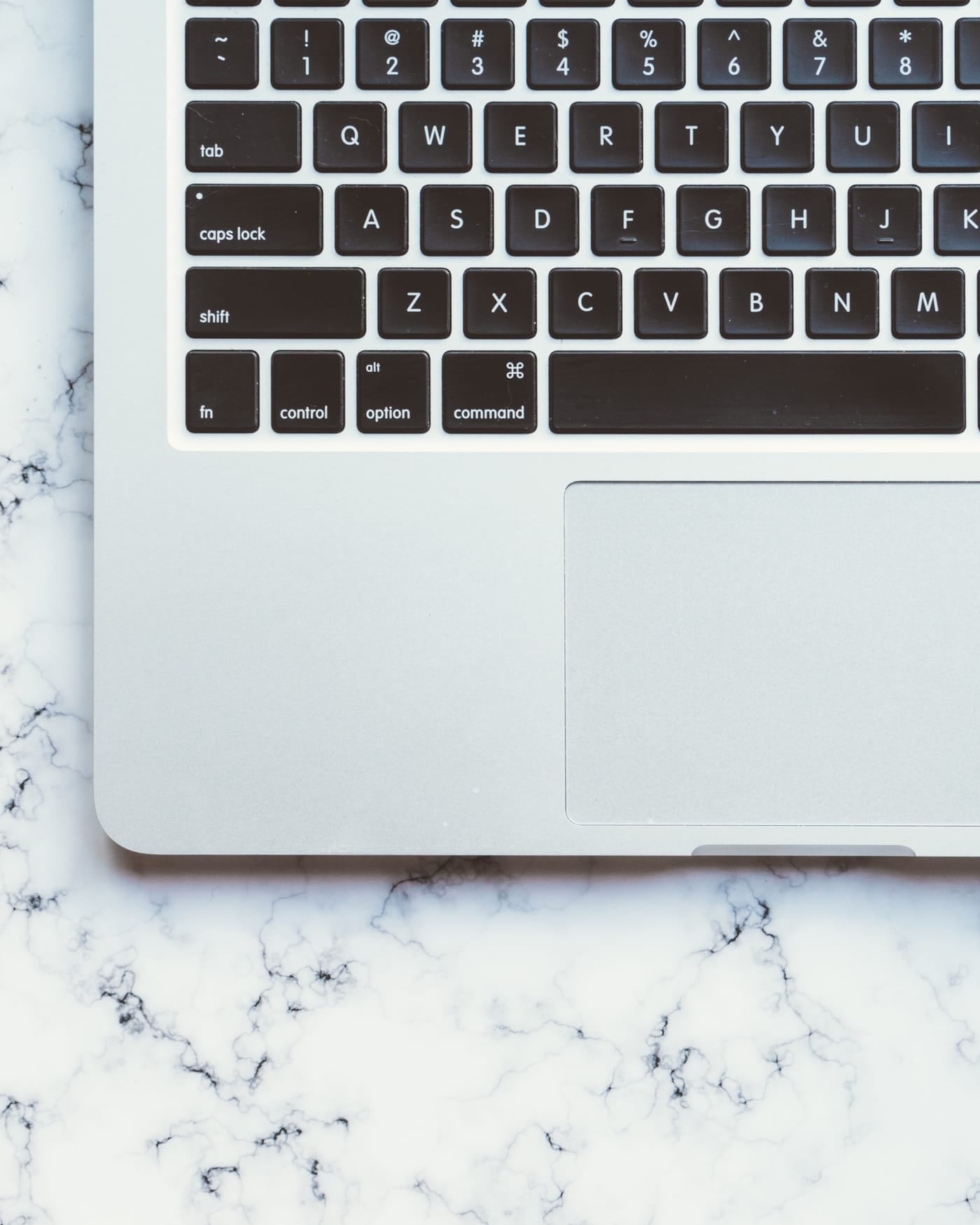 Silver laptop keyboard and trackpad lying on a white marble surface