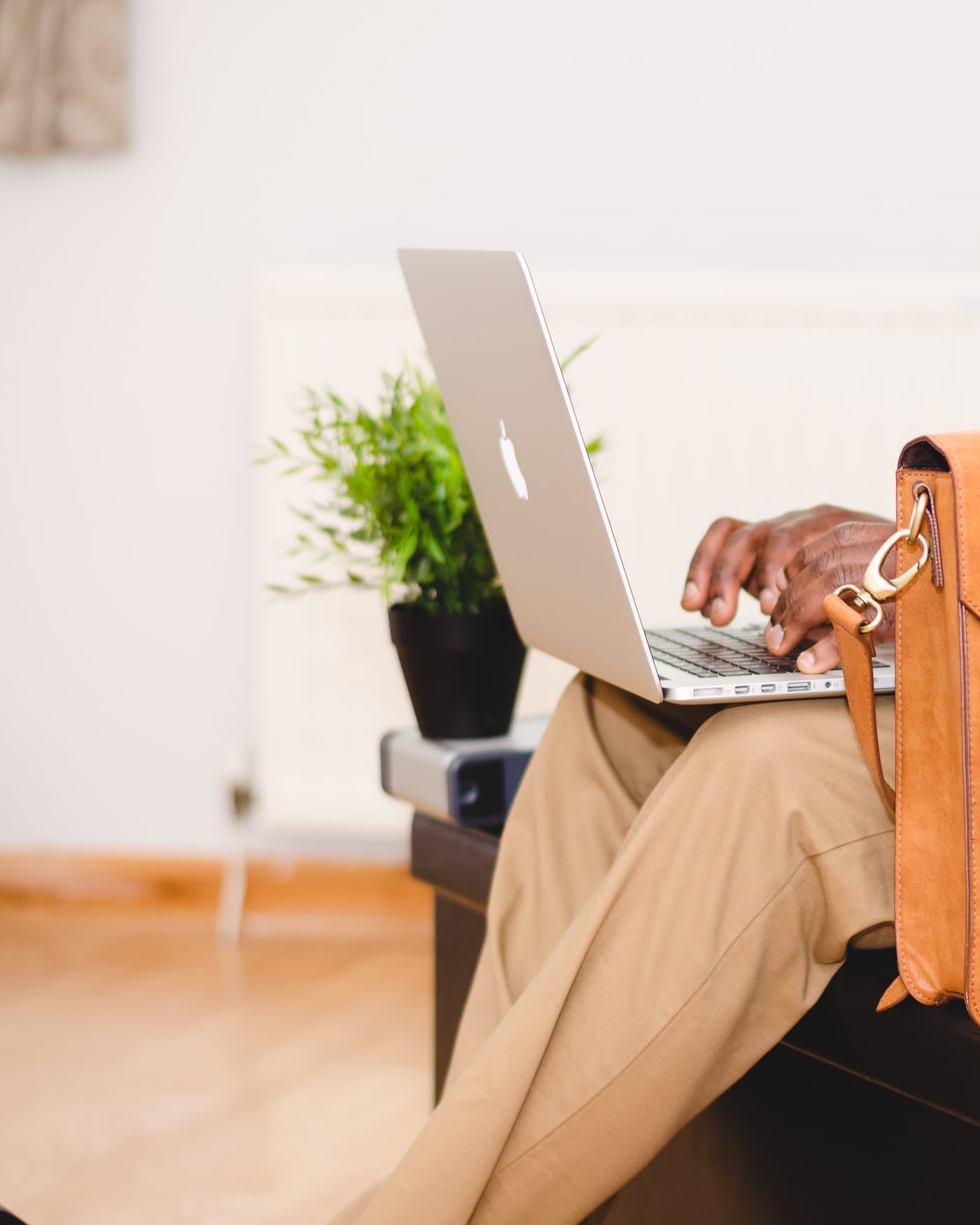 Man in a navy blazer working on a laptop with a tan leather briefcase beside him